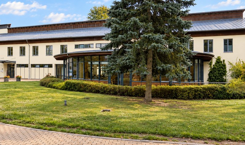 Fachklinik Heidehof in Weinböhla: Klinikgebäude mit runder Glasfront, großer Tanne und Rasen